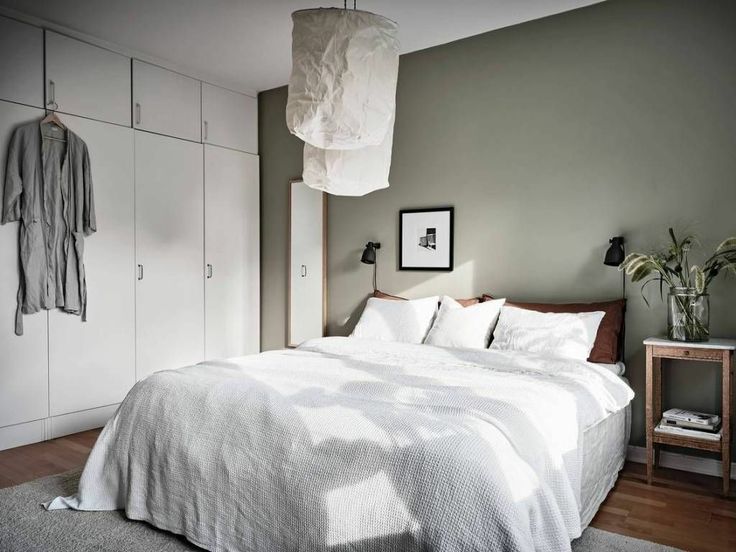 a white bed sitting in a bedroom next to a wooden table and lamp on top of a hard wood floor