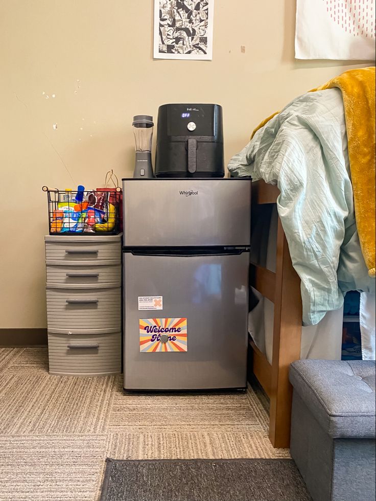 a room with a bed, desk and two refrigerators next to each other in it