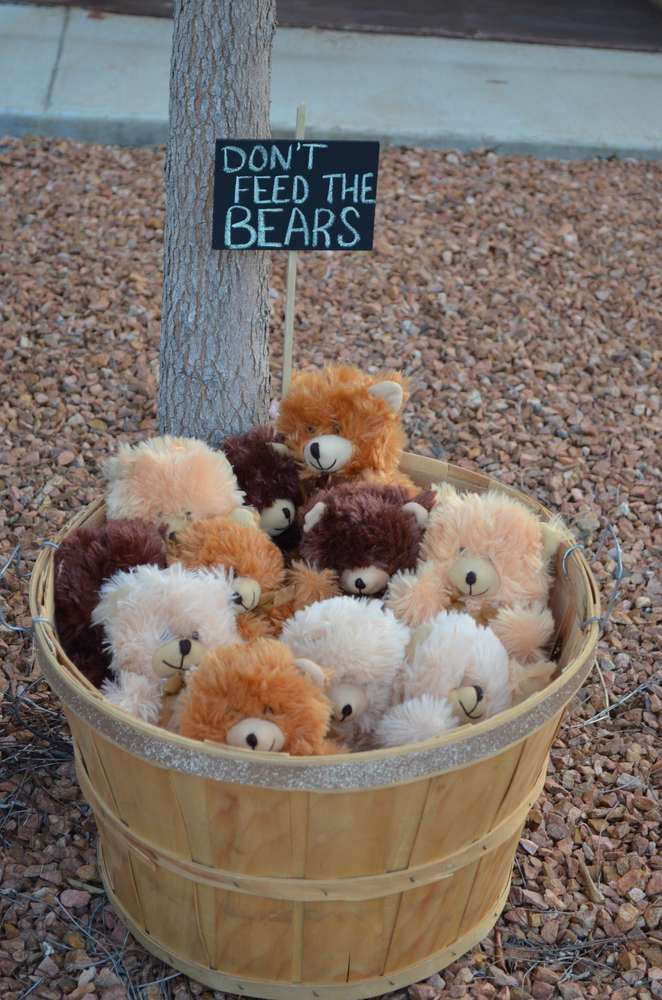 a basket full of stuffed animals sitting under a tree with a sign that says don't feed the bears