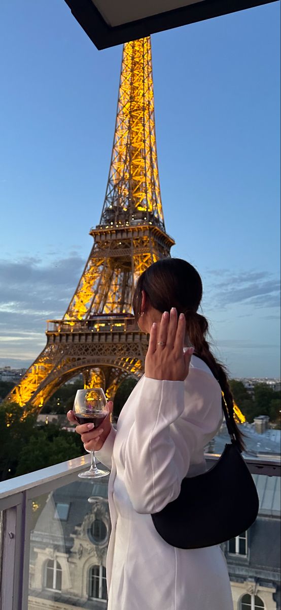 a woman standing in front of the eiffel tower holding a glass of wine