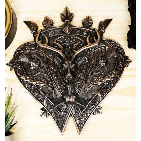 a decorative metal heart with an animal head in the center on a wooden surface next to a plant