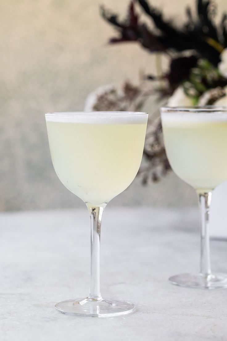 two glasses filled with white wine sitting next to each other on top of a table