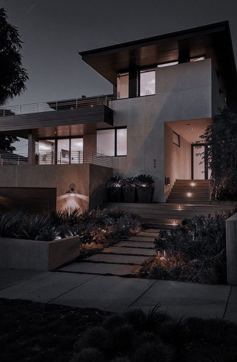 a modern house lit up at night with lights on the windows and steps leading to it