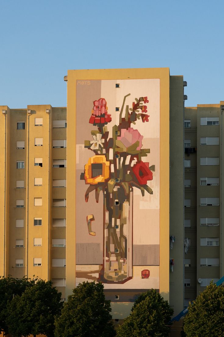 a tall building with a painting on it's side and flowers in a vase