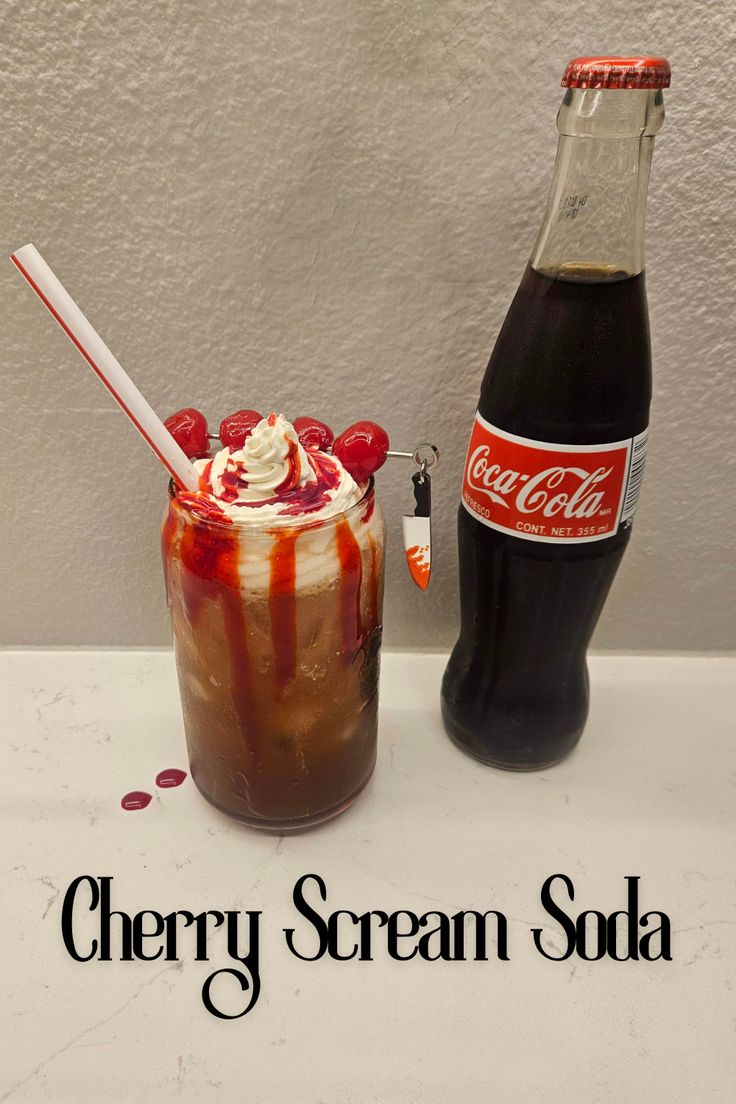 there is a drink with whipped cream and cherries in it next to a coke bottle