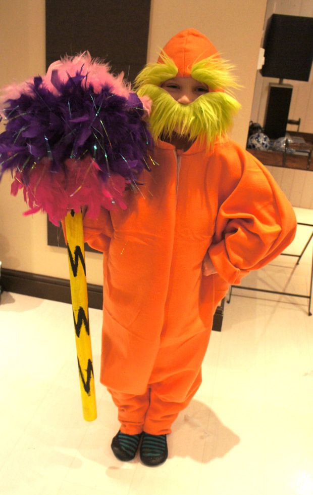 a child dressed in an orange costume holding a large purple and yellow feathered stick