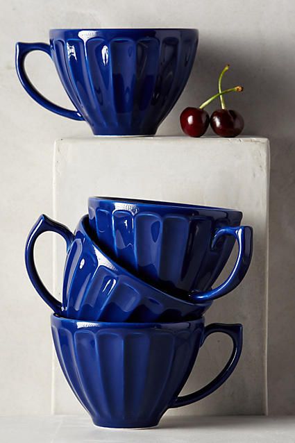 three blue coffee cups stacked on top of each other with cherries in the background