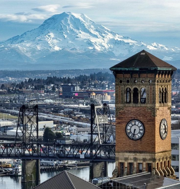 a tall clock tower sitting in the middle of a city next to a snow covered mountain