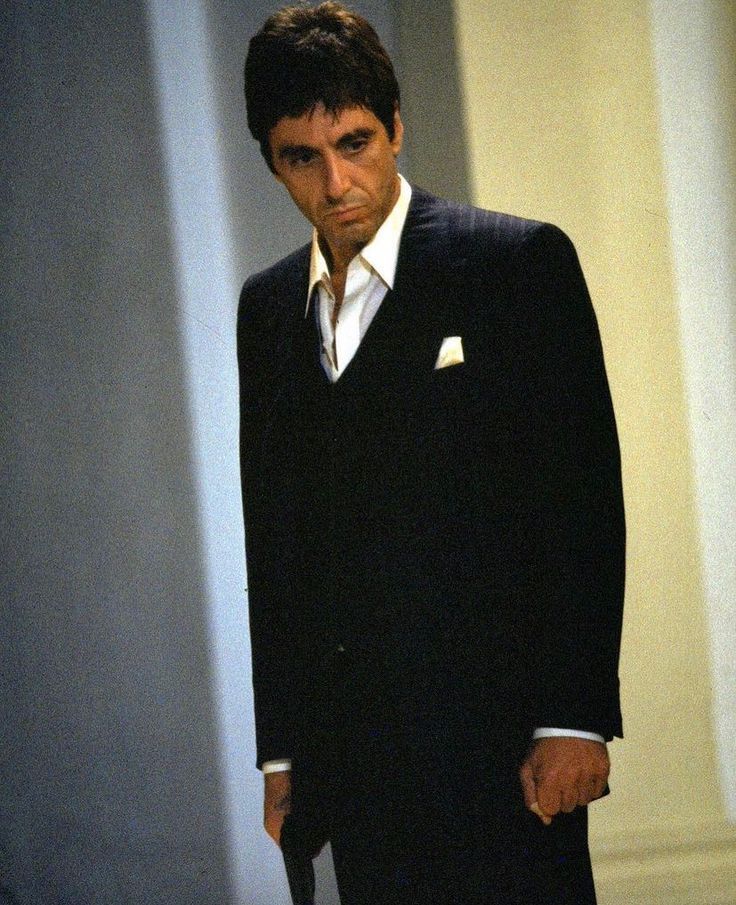 a man in a suit and tie standing next to a white wall with his hand on his hip