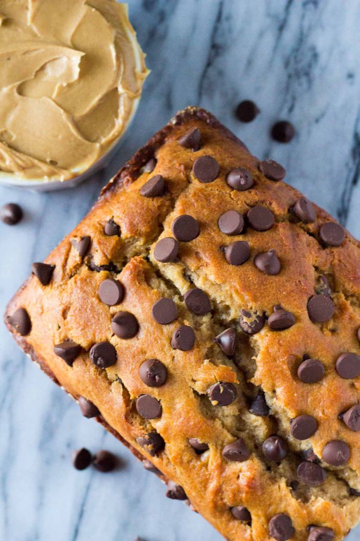 a loaf of chocolate chip banana bread next to a bowl of peanut butter on a marble surface