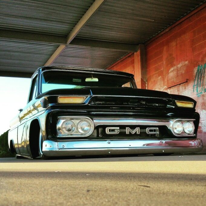 an old black pickup truck parked under a bridge