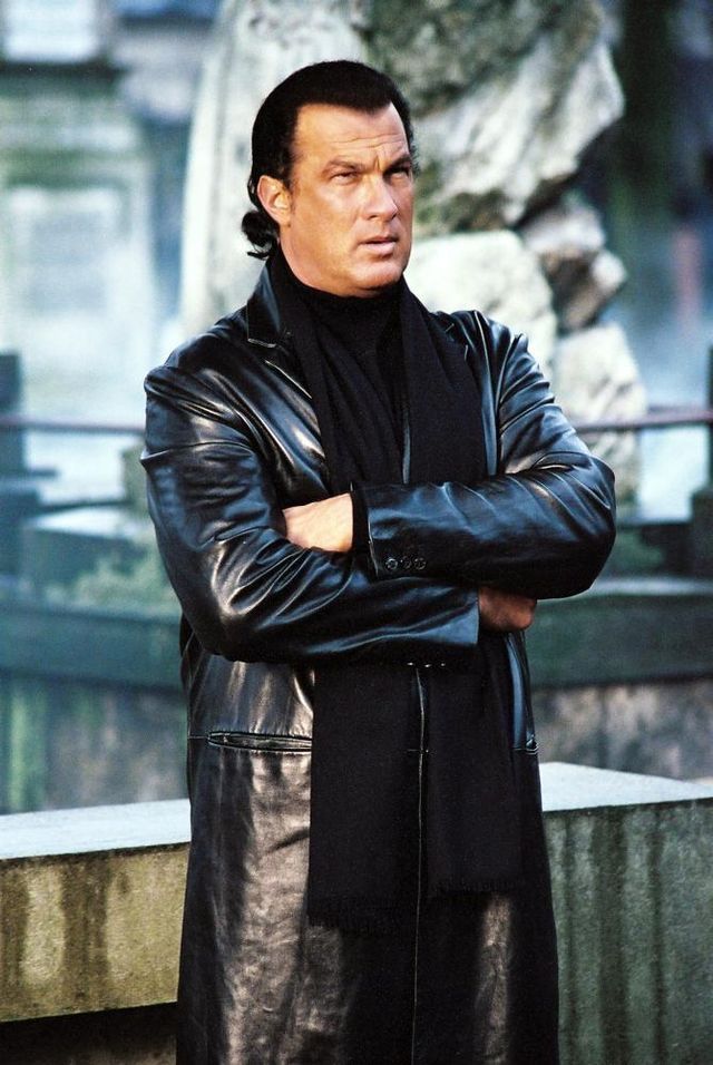 a man wearing a black leather coat standing with his arms crossed