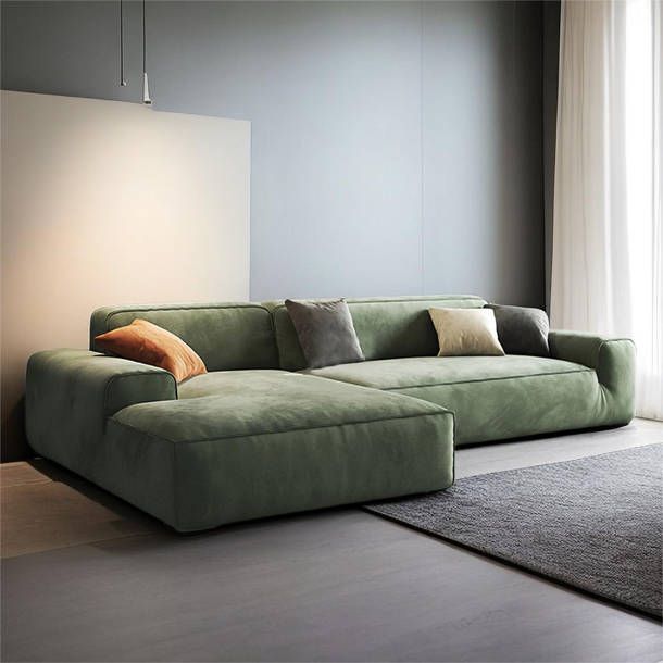 a large green couch sitting in front of a window next to a rug and lamp