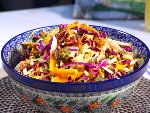 a colorful salad in a blue bowl sitting on a table next to a glass of orange juice