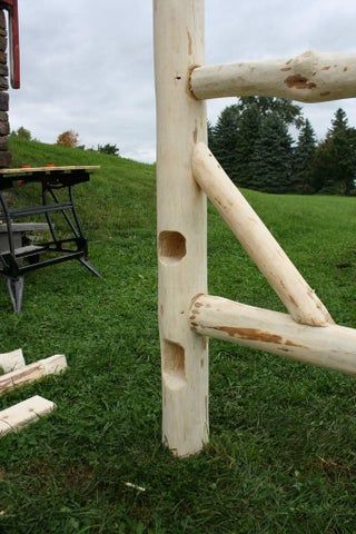 a wooden fence made out of logs in the grass near a picnic table and bench