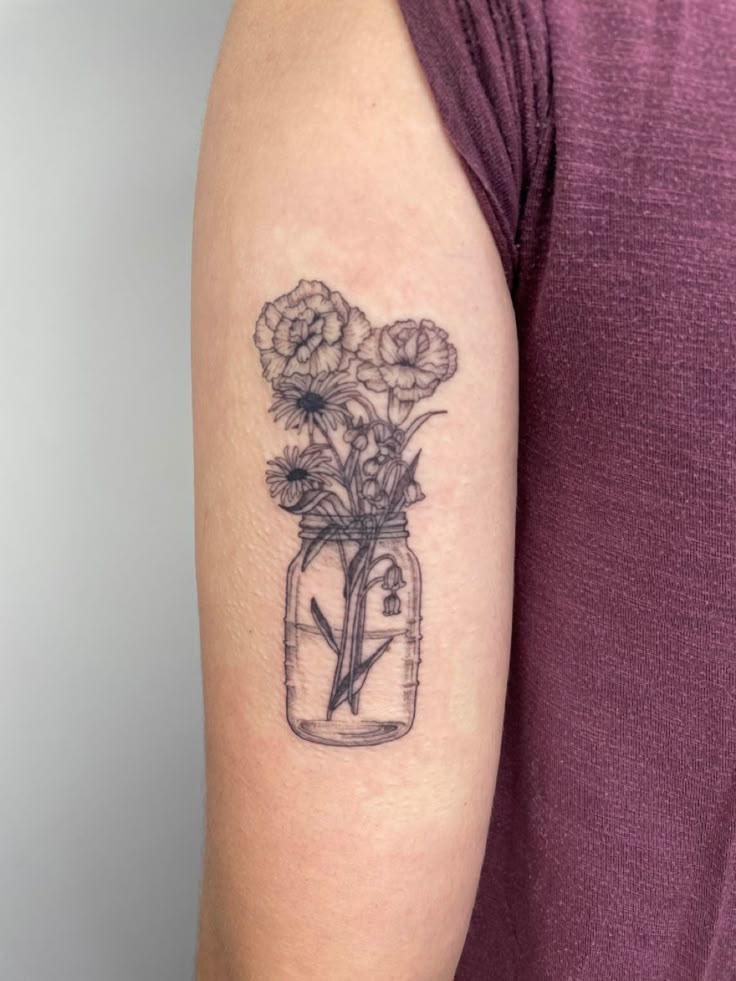 a woman's arm with flowers in a mason jar tattoo on the left upper arm