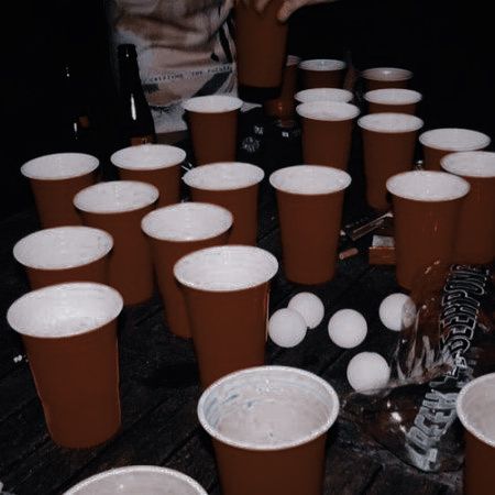 many plastic cups are lined up on the table with one person reaching for something in front of them