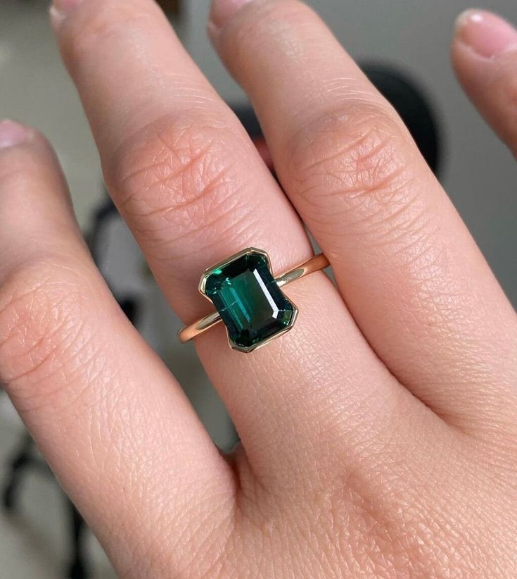 a woman's hand with a green ring on top of her finger and an emerald stone in the middle