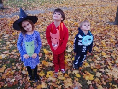 three children dressed up in halloween costumes standing on the ground with leaves all around them