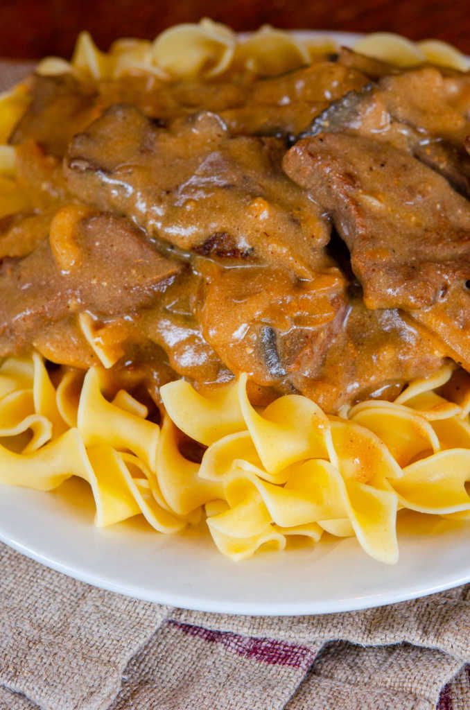 a white plate topped with pasta and meat covered in gravy on top of a table