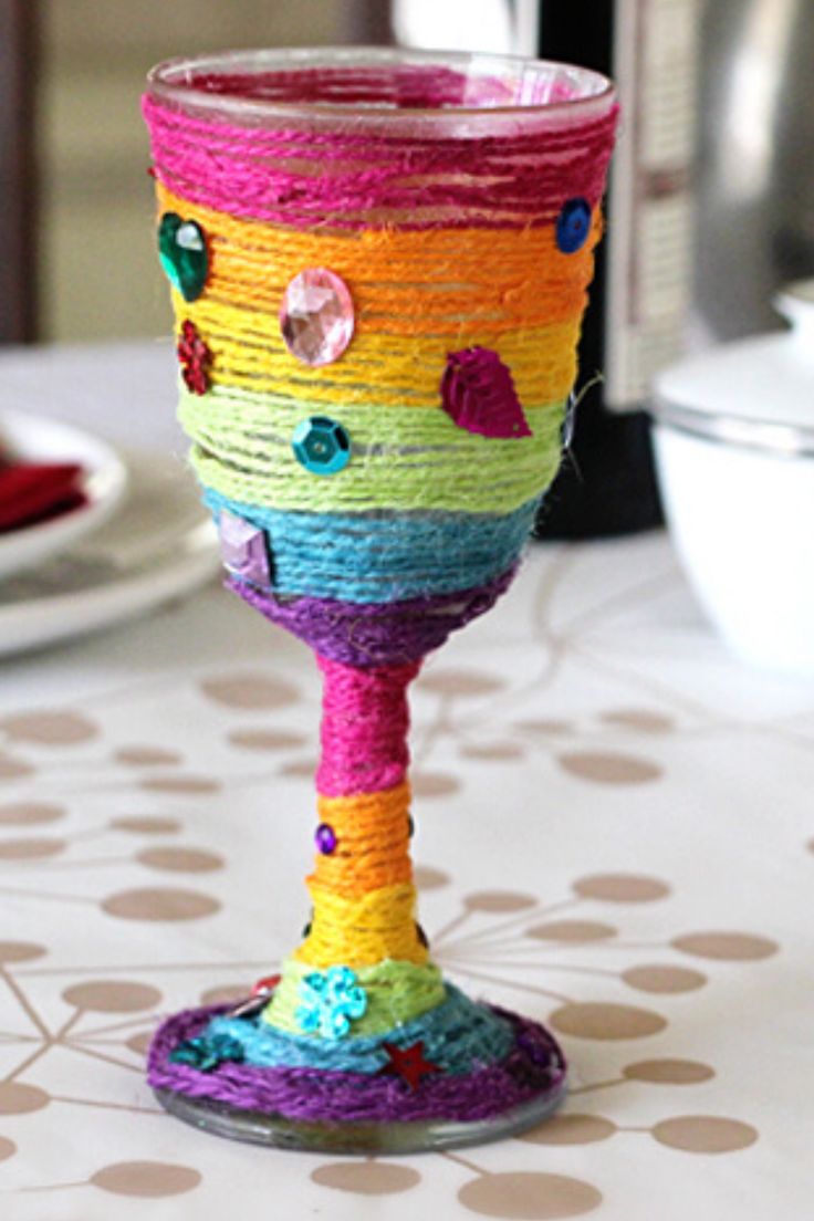 a colorful wine glass sitting on top of a table next to a plate and bowl