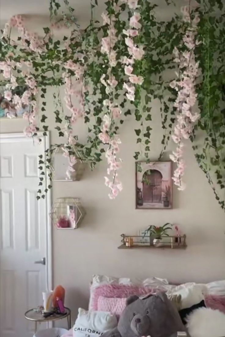 a bedroom with pink flowers hanging from the ceiling and stuffed animals on the bed in front of it