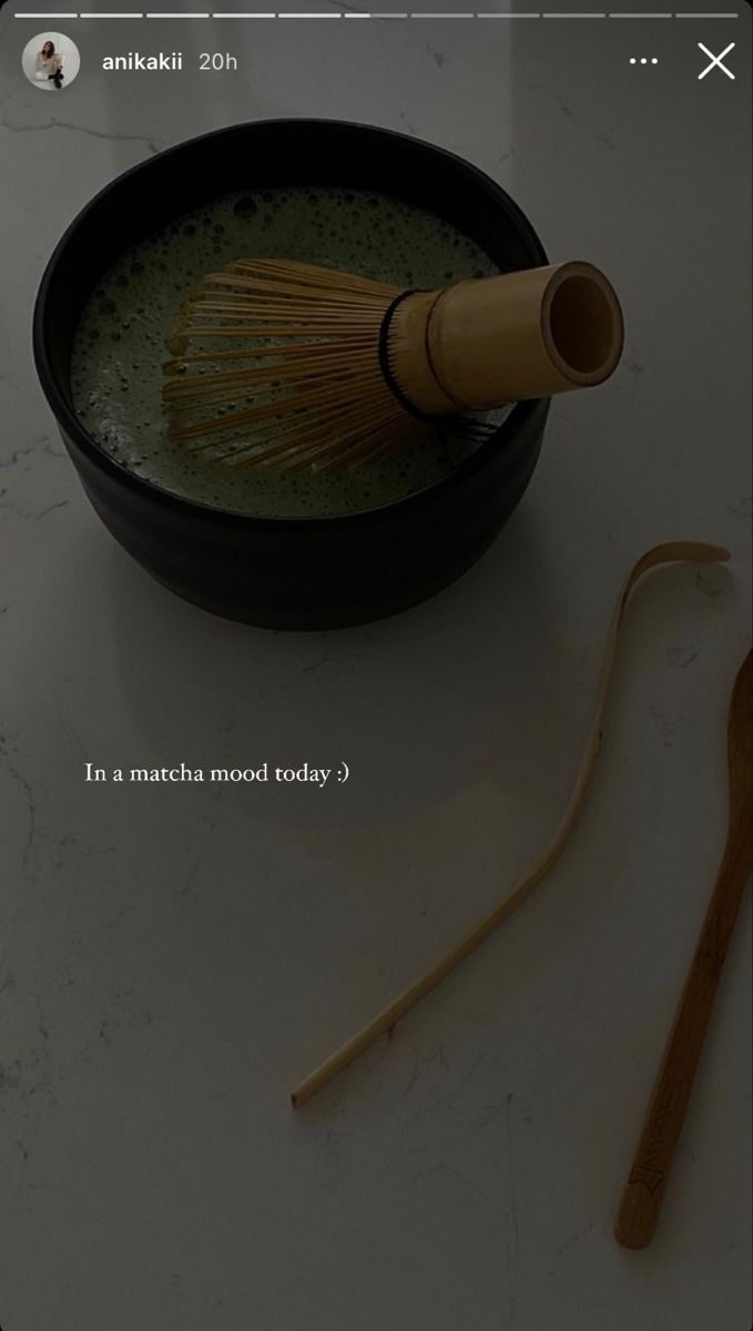 a wooden whisk in a black bowl next to a bamboo spoon on a white counter