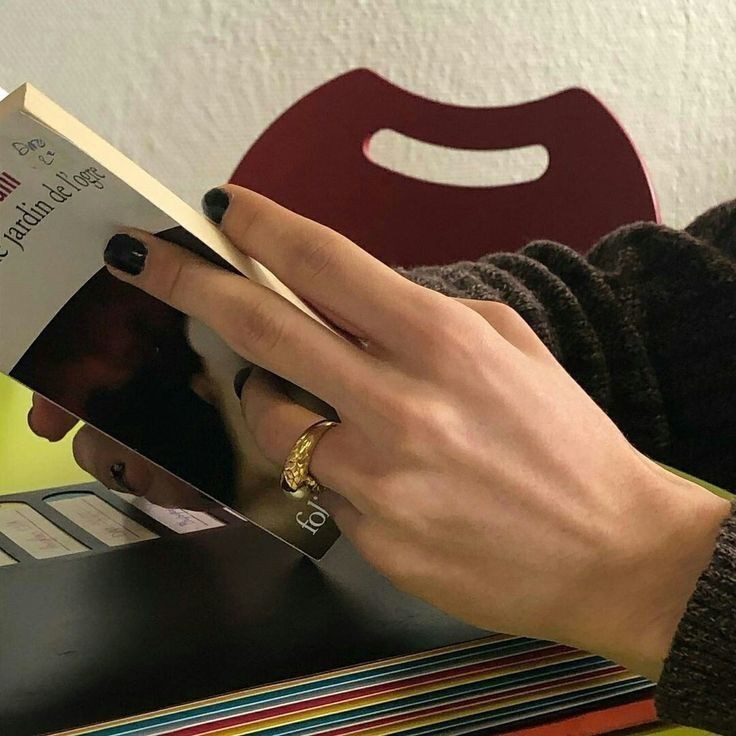 a woman is reading a book with her hands on top of the book and holding it in one hand