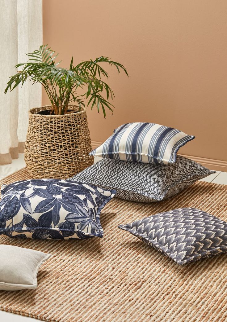 four pillows are on the floor next to a potted plant and a wicker basket