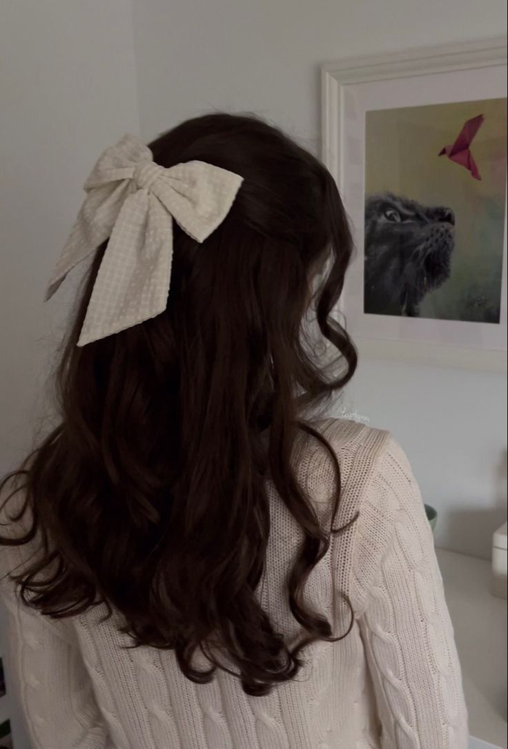 a woman with long hair wearing a white sweater and a large bow in her hair