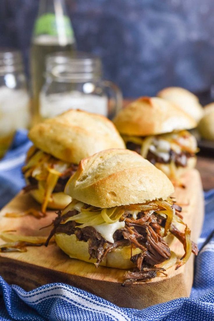 three pulled pork sandwiches on a wooden cutting board with blue and white towel next to them