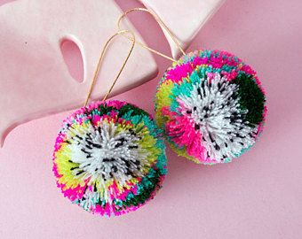 a pair of colorful earrings sitting on top of a pink table next to a white bag