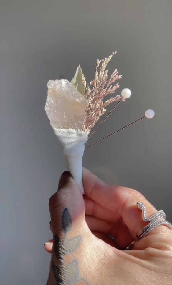 a hand holding a small white vase with flowers on it's tip and two pins sticking out of it