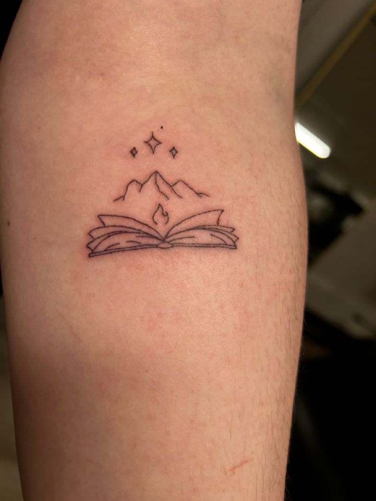 an open book with mountains and stars on the cover up is sitting on someone's leg