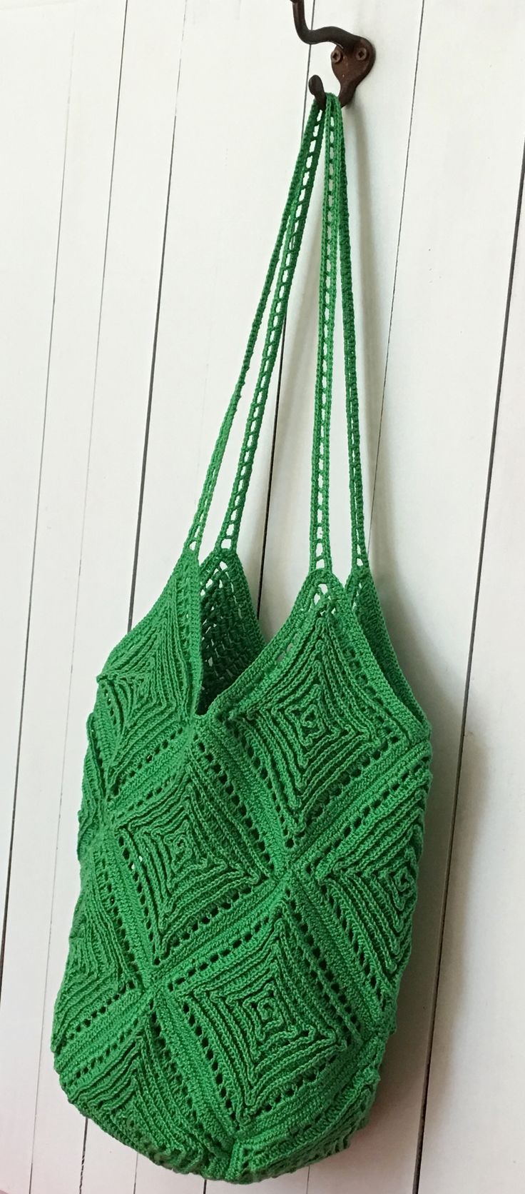 a green crocheted bag hanging from a hook on a white wooden wall,