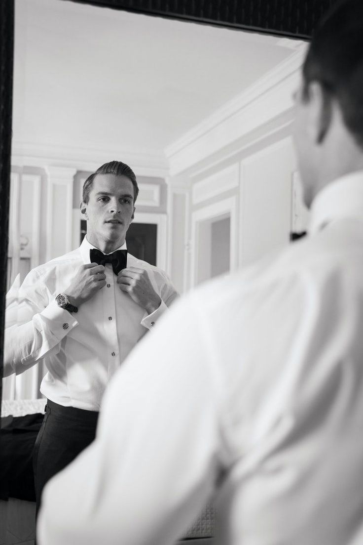 a young man adjusting his bow tie in front of a mirror