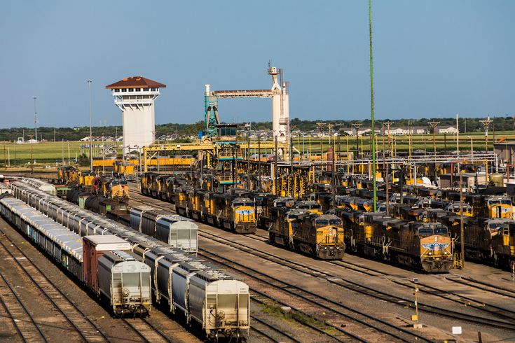 many trains are parked on the tracks near each other in an industrial area with a control tower in the background