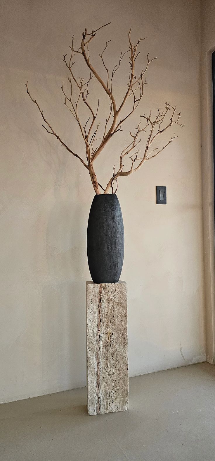 a black vase with branches in it sitting on top of a stone block next to a window