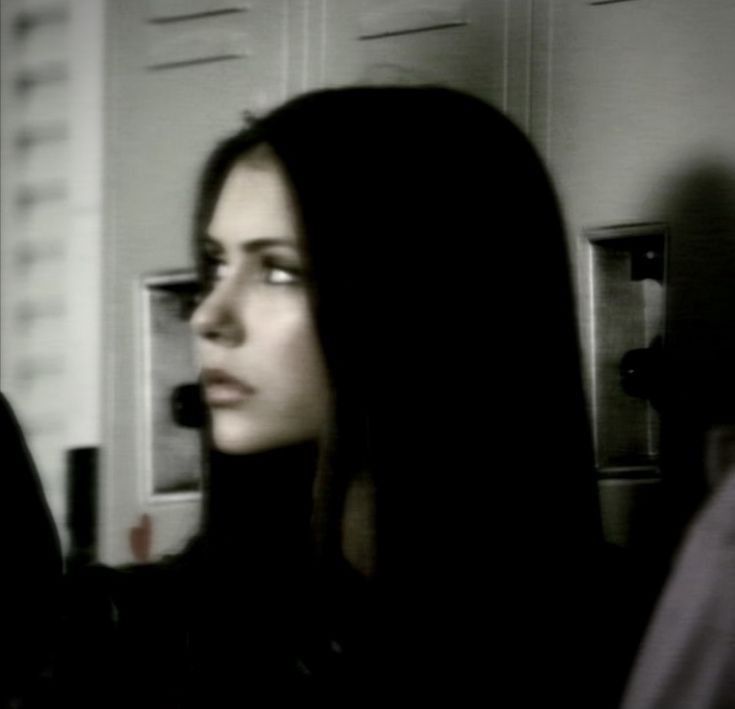 a woman with long black hair standing in front of a microwave and looking off into the distance