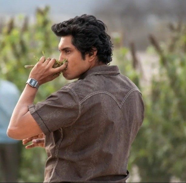 a man eating something with his hands while standing in front of some bushes and trees