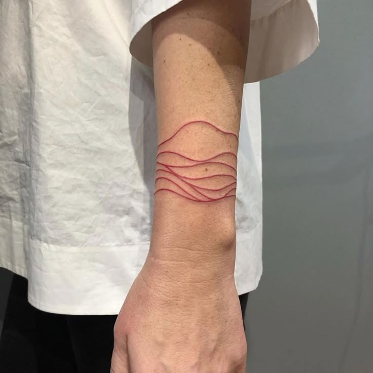 a person's arm with a red wave tattoo on the left side of their wrist