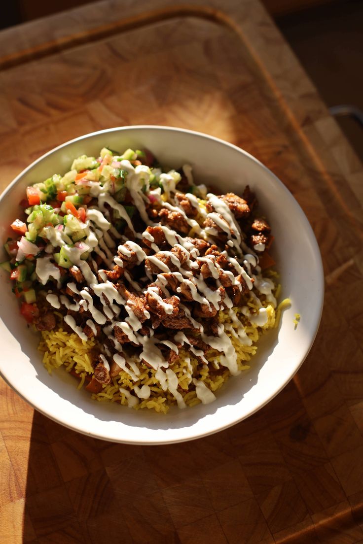 a white bowl filled with rice and meat covered in dressings on top of a wooden table