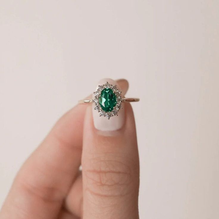 a woman's hand holding a ring with an emerald and diamond center stone on it