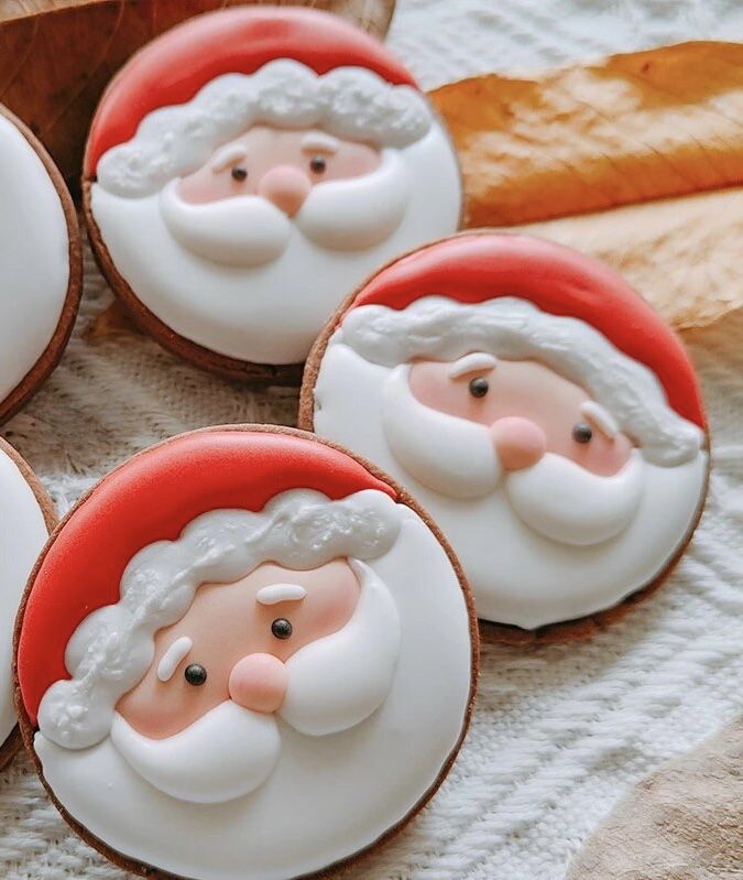 four decorated cookies with santa claus faces on them, sitting on a table next to leaves