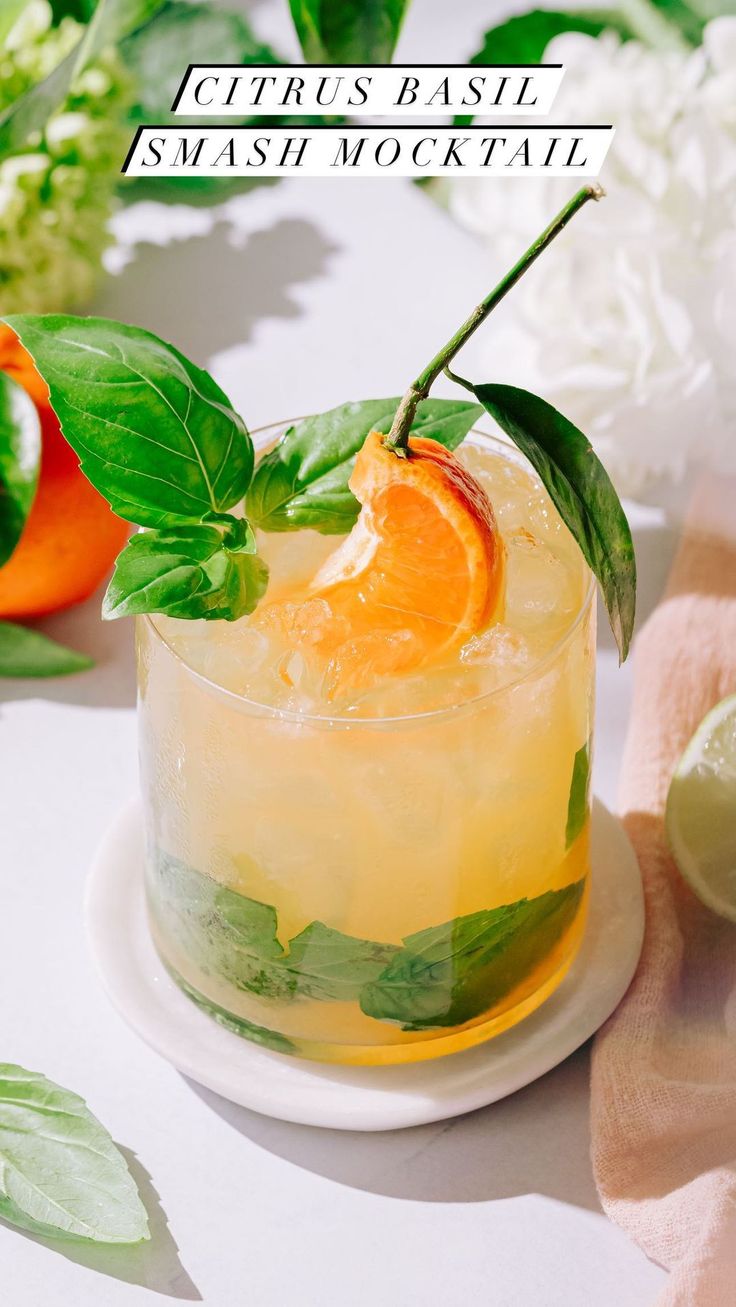 an orange and basil cocktail on a white plate next to some green leaves, limes and flowers