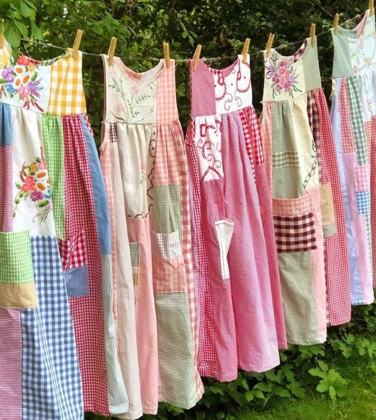 many different colored dresses hanging on a clothesline in front of some trees and bushes