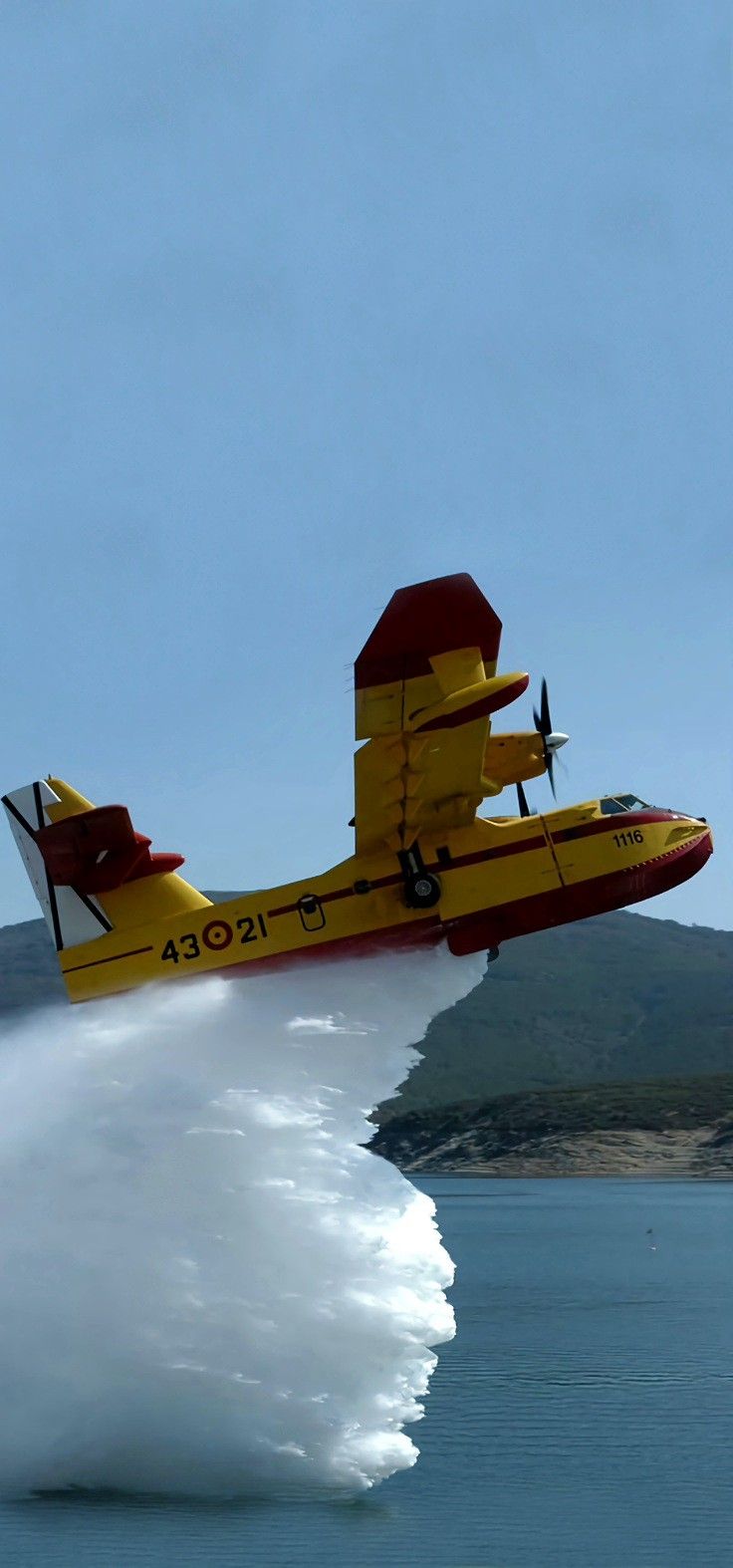 a yellow and red plane is flying over the water with it's landing gear down