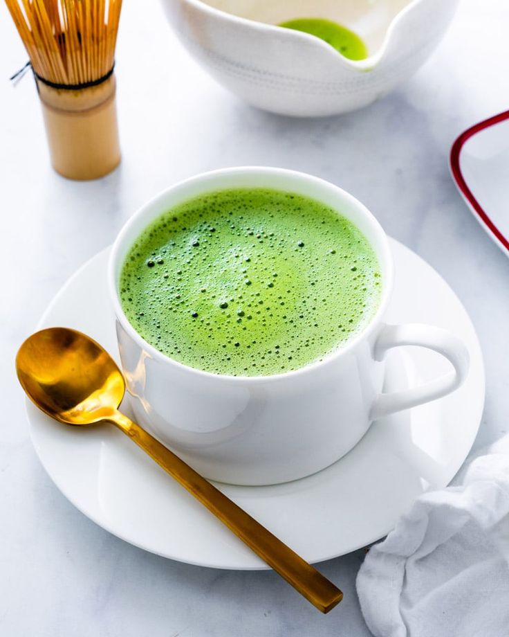 a cup of green tea on a saucer with a spoon next to the bowl