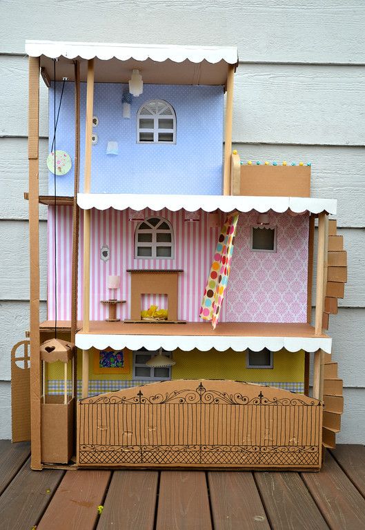 a doll house made out of cardboard on top of a wooden deck with stairs leading up to the second floor