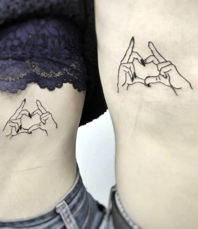 two people with tattoos on their stomachs are holding hands and making the shape of a heart